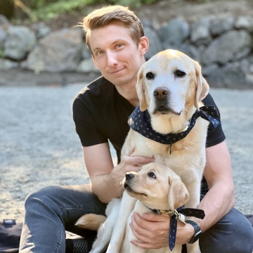 Brian with two yellow English Labradors, one a senior and one a puppy